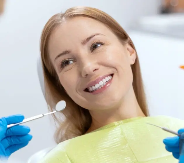 Smiling female patient in dental chair during professional cleaning appointment.