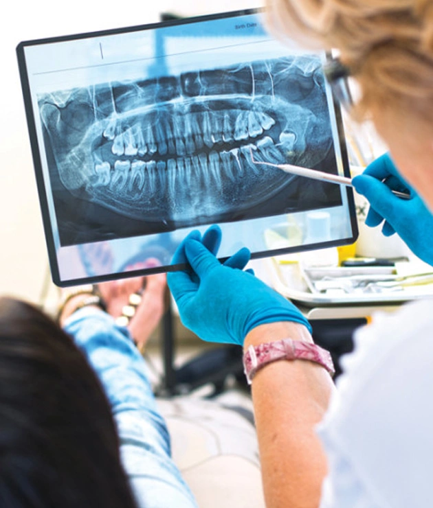 Dentist examining panoramic X-ray with patient, wearing blue gloves in clinical setting.