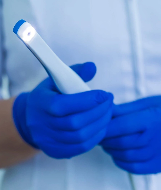 Dental professional in blue gloves holding intraoral camera in clinical setting.