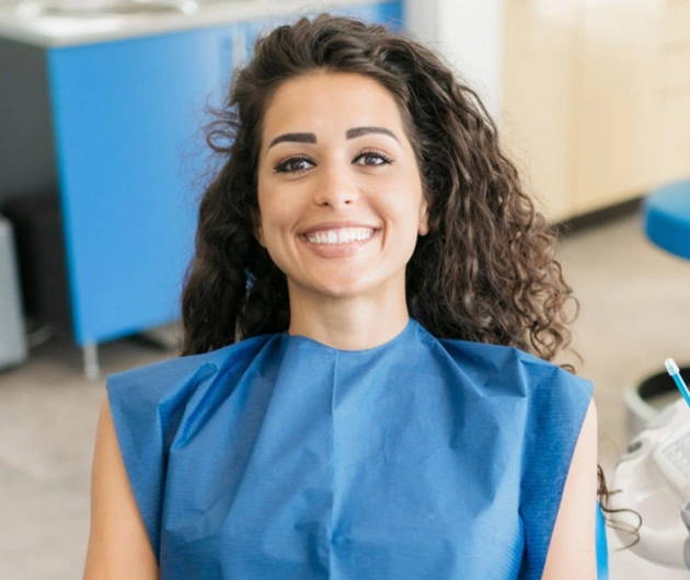 Smiling woman in blue medical scrubs in a dental office setting.