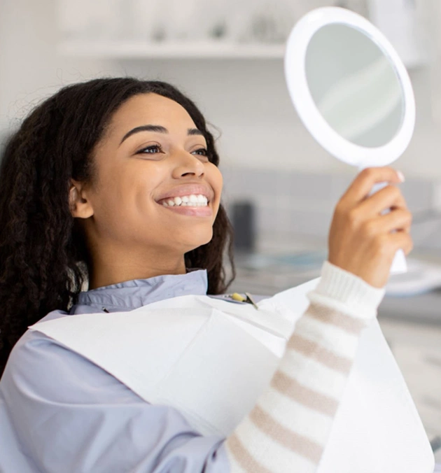 Woman smiling while holding illuminated mirror in modern dental office setting