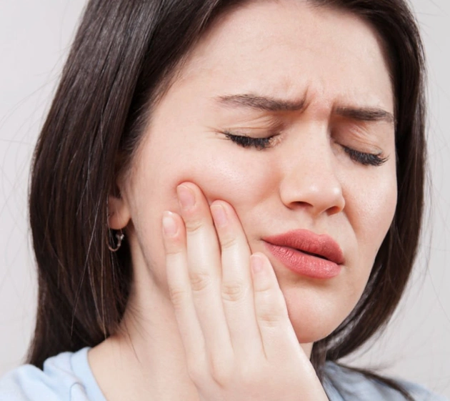 Woman holding cheek in pain, eyes closed, expressing dental discomfort or toothache.