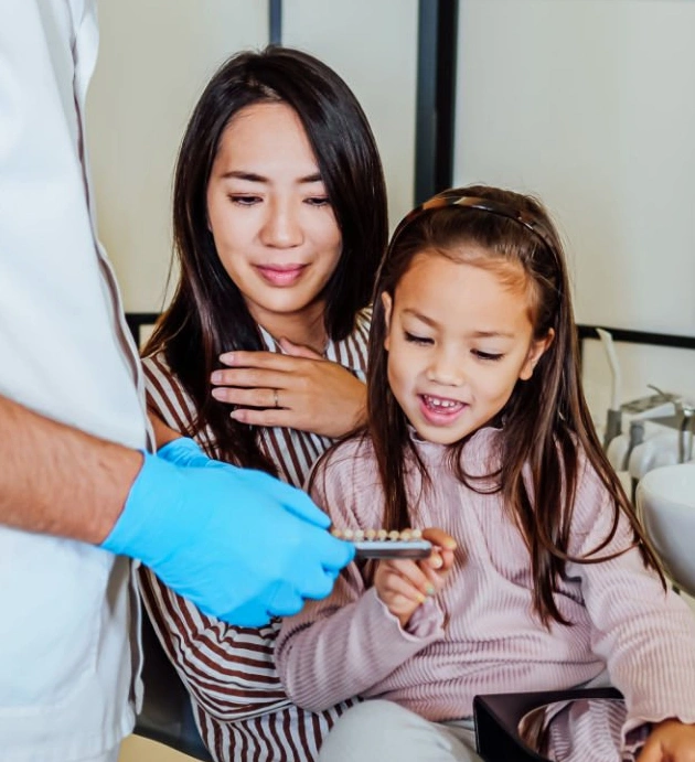 Woman and young child examining blue dental model with dentist in clinical setting.