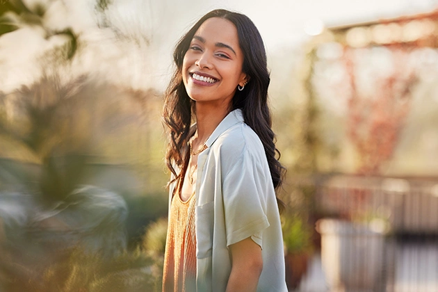 Smiling woman in casual light clothing outdoors during golden hour with blurred urban background