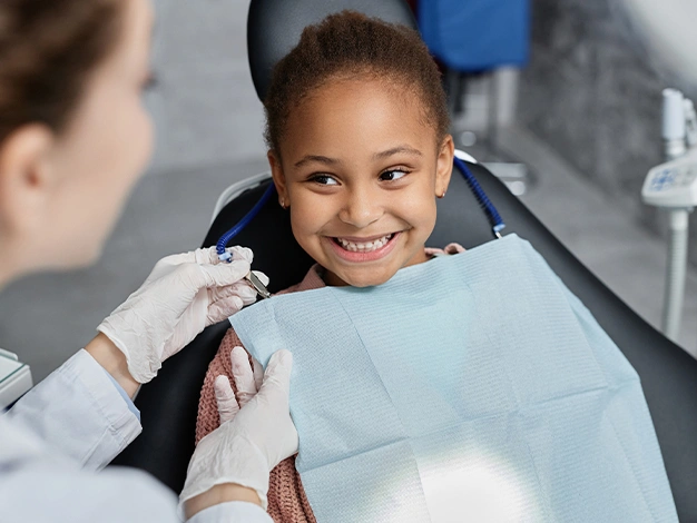 Young girl smiling at dental appointment while dentist shows her intraoral mirror in clinical setting.