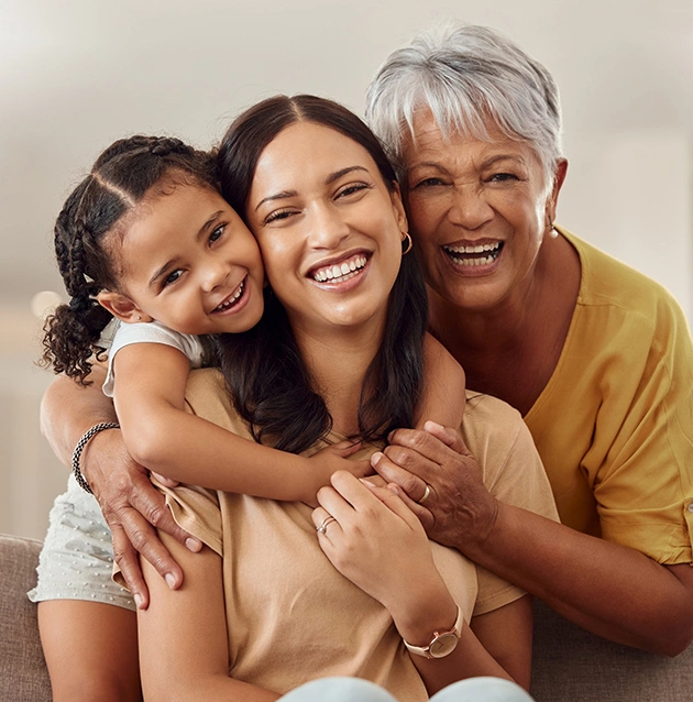 Three generations of women smiling together in a warm family portrait indoors.