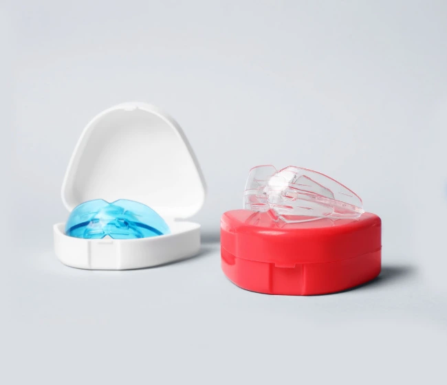 Two open dental retainer cases with blue and pink colored retainers inside on white background.