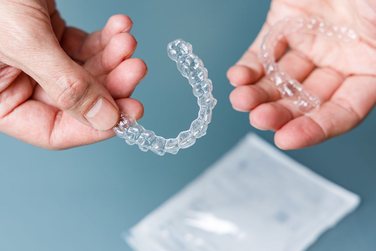 Hands holding clear Invisalign aligners demonstrating proper care and handling habits.